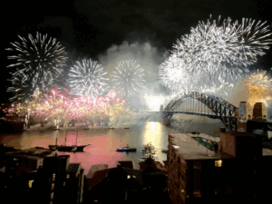 Fireworks explode in silver, pink and gold over the Sydney Harbour bridge and are reflected in the harbour.